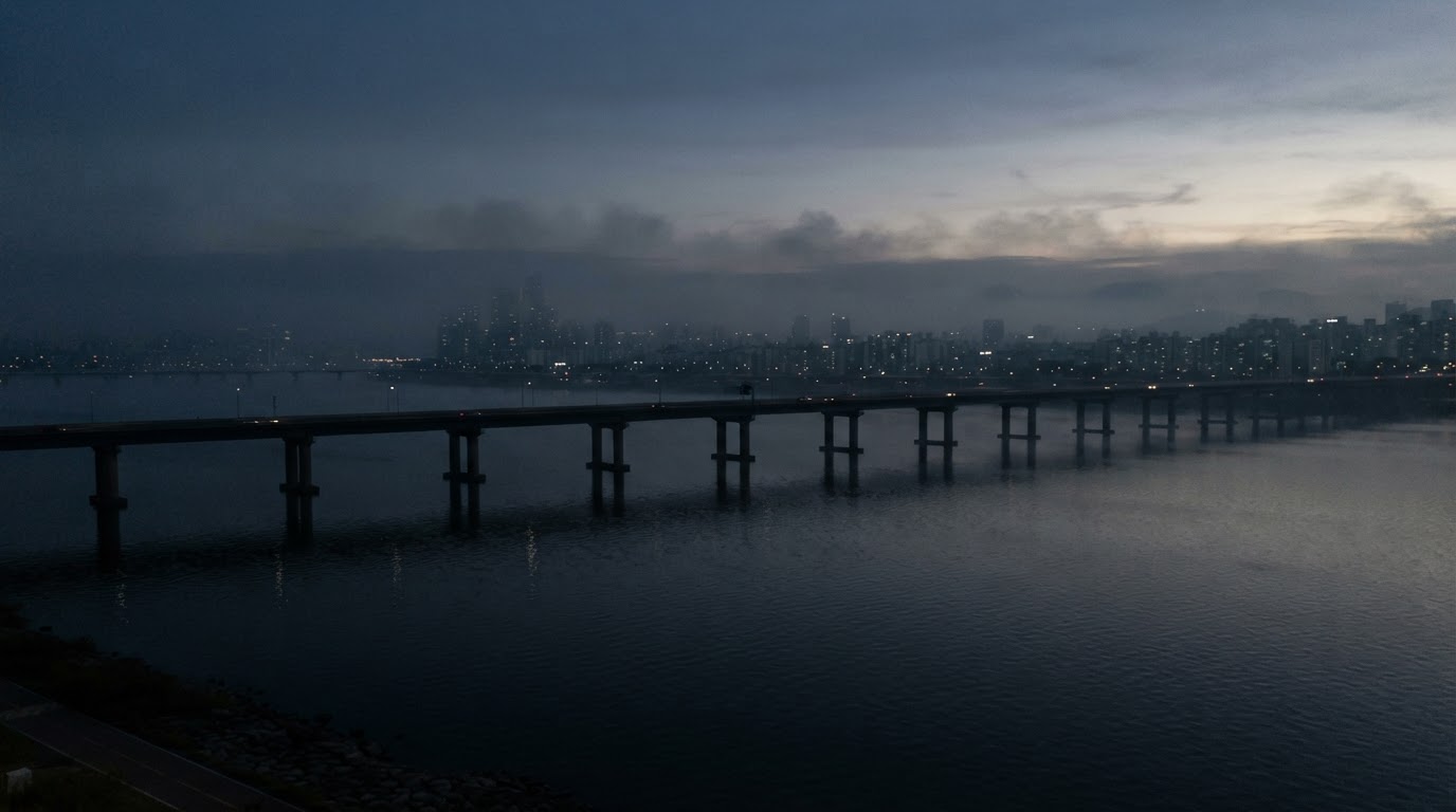 The silhouette of the Han River and a bridge at dawn. A thin mist lies over the water.