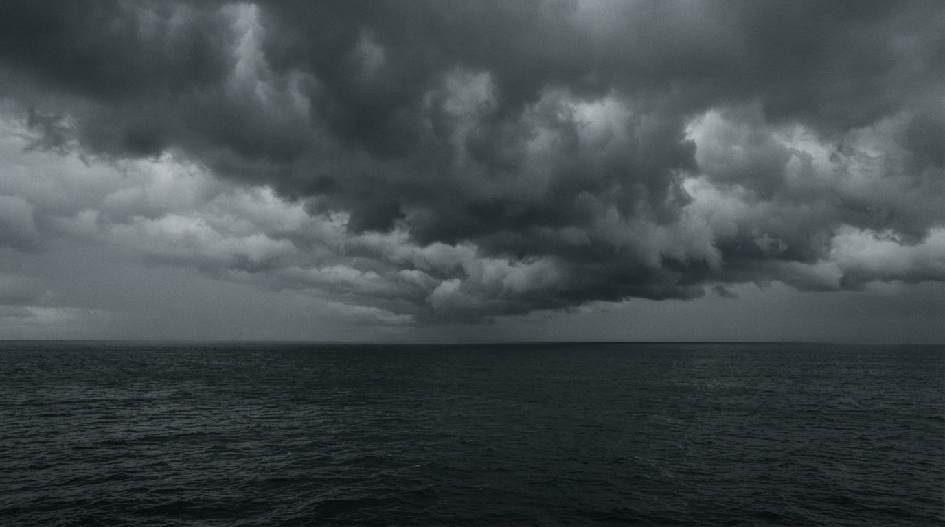 Storm clouds massing over a flat, waiting sea, the light gone heavy and grey