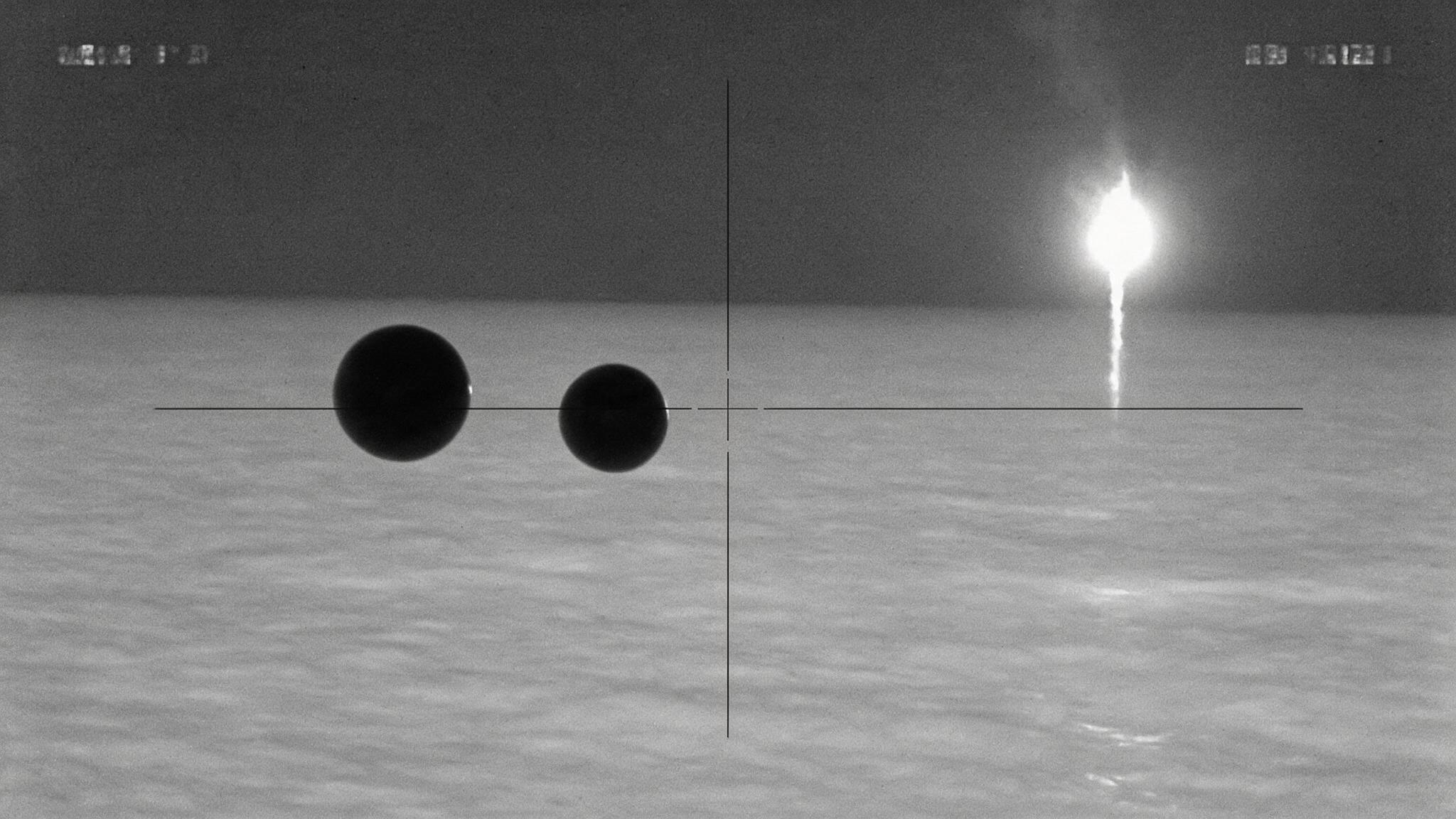 Infrared thermal view: two cold, dark spheres hovering low over the sea at night, showing no heat signature. (AI-generated reconstruction of the described infrared footage)