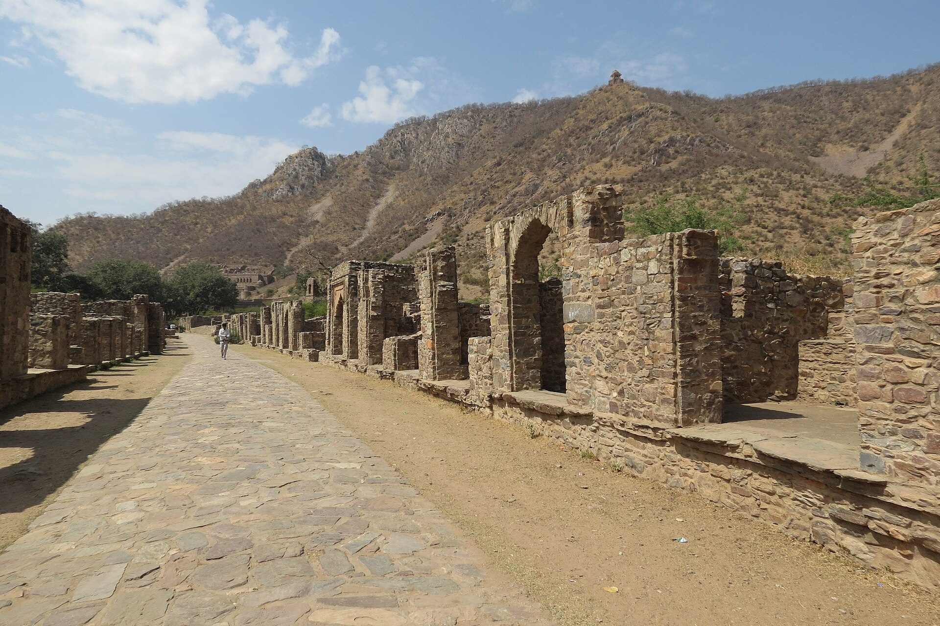 Collapsed stone colonnades along the processional path, with the ridges of the Aravalli range behind