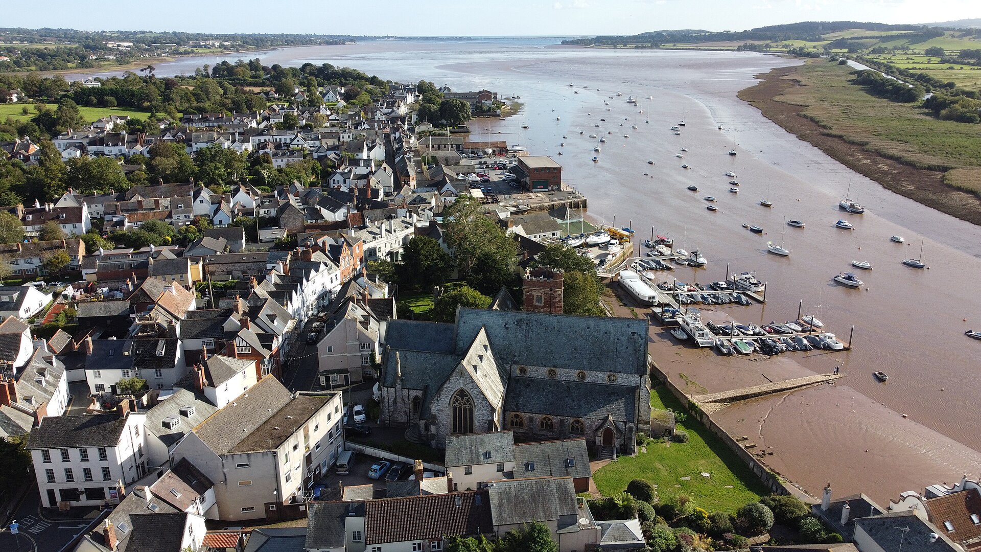 Topsham seen from the air today, its roofs and garden walls packed tightly together with the Exe estuary beyond — one of the villages where the 1855 trail was said to have climbed over rooftops and walls.