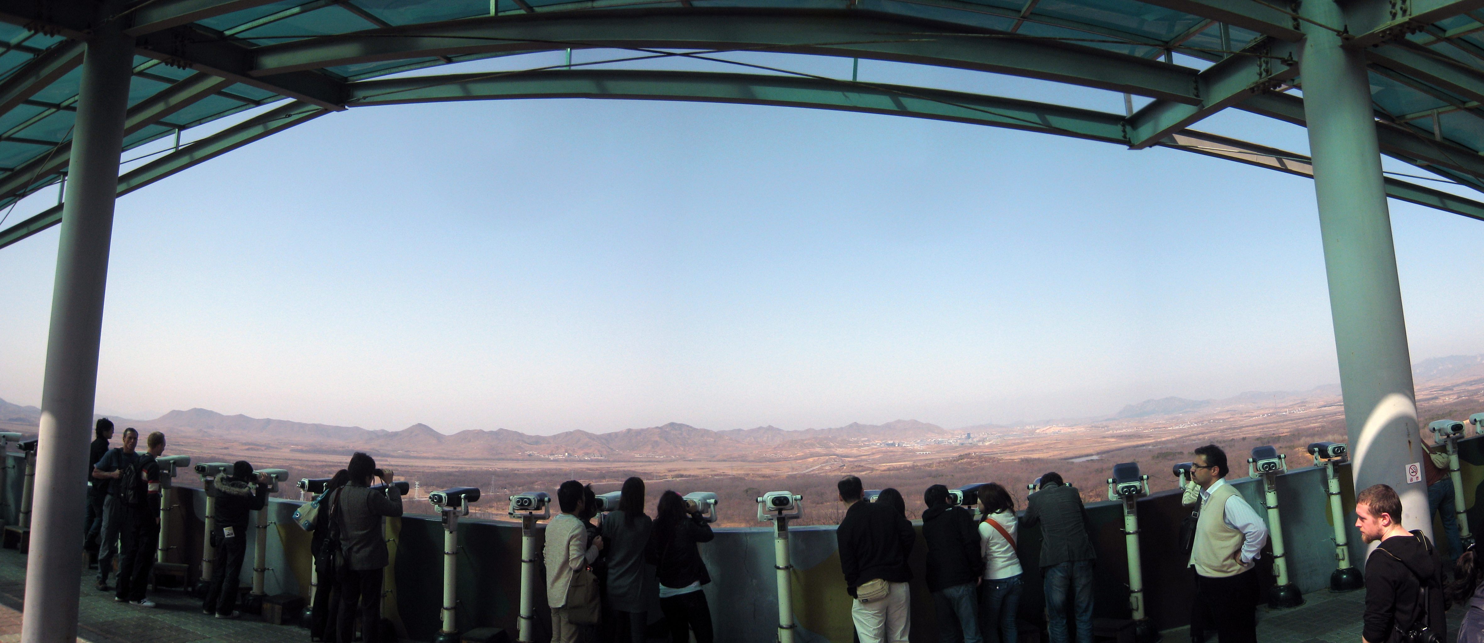 People looking north from an observatory — beyond the binoculars, the village will light up on time again tonight.