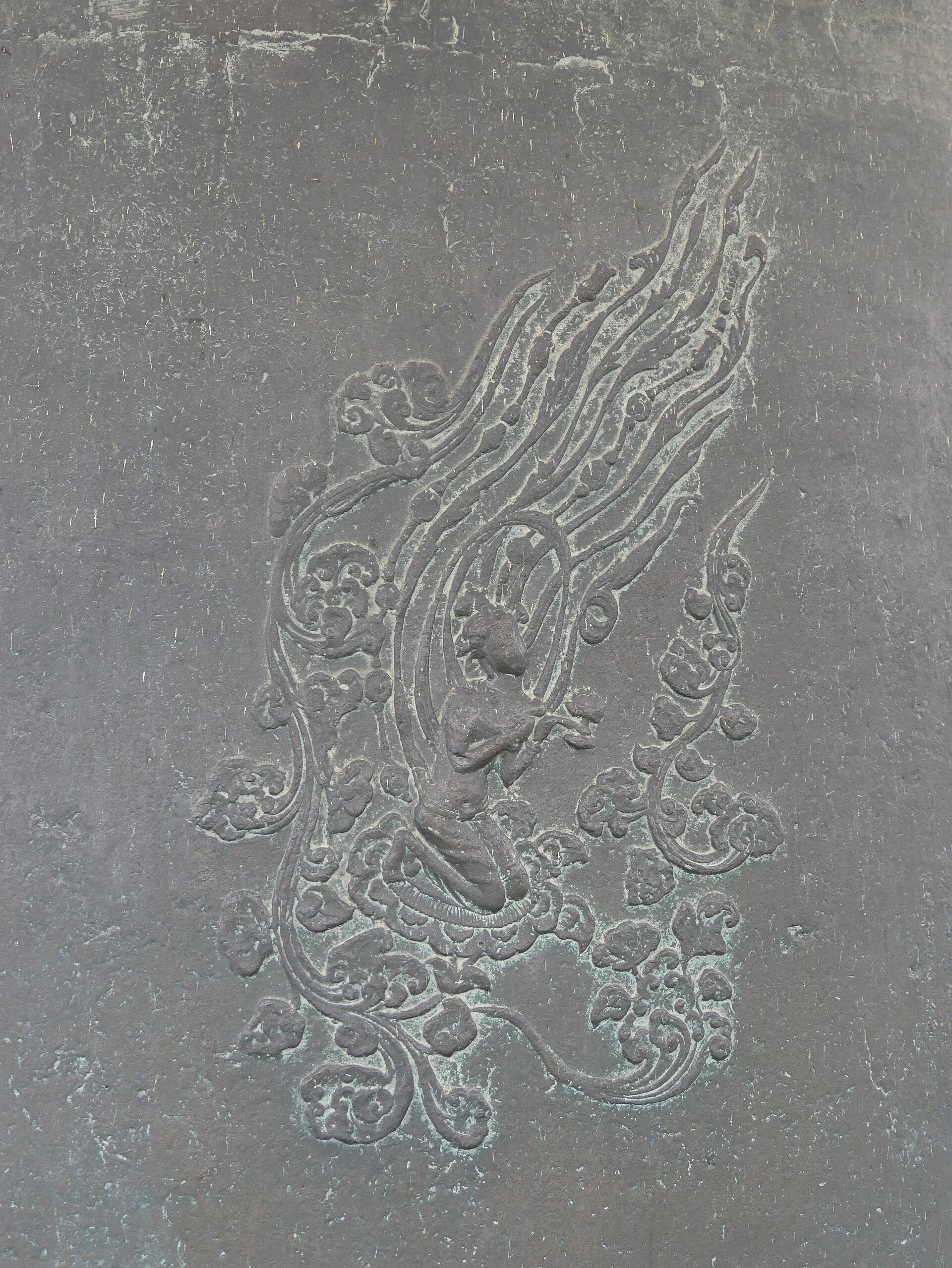 Close-up of an apsara relief cast into the surface of the bell — a celestial figure kneeling on a cloud
