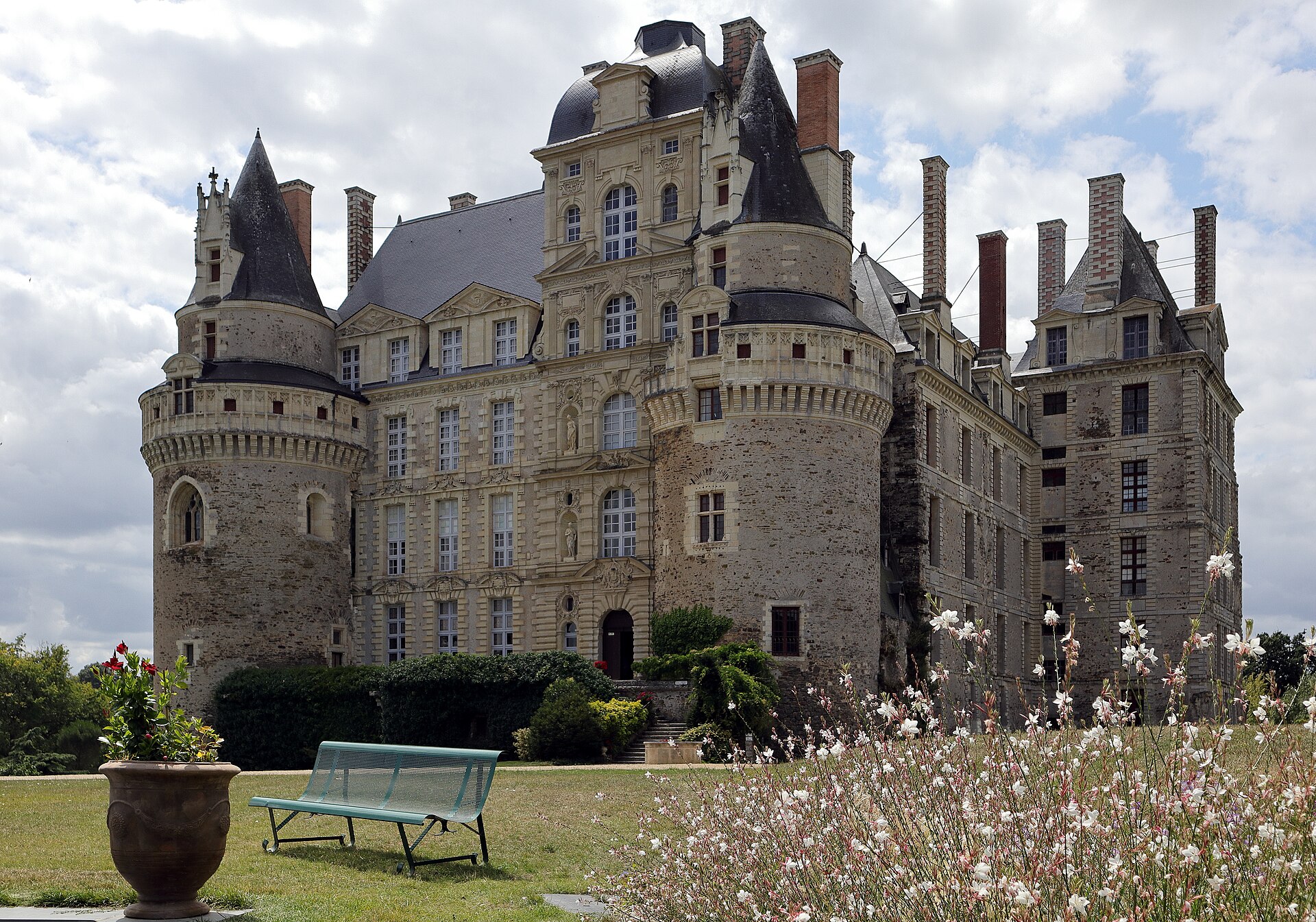 The front façade of the Château de Brissac as it stands today in the Anjou country of France, flanked by conical-roofed towers with chimneys ranged along the roofline.