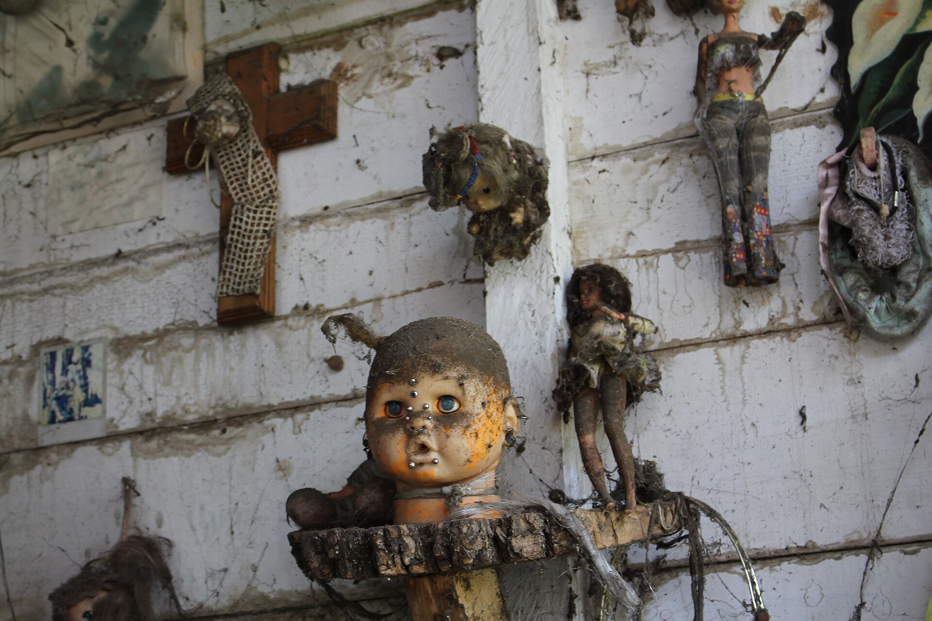 Weathered dolls nailed to a plank wall with a cross standing among them — the Island of the Dolls today