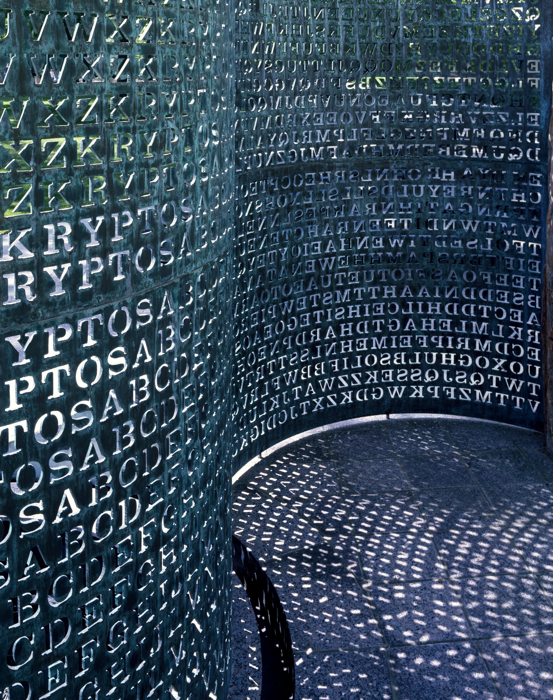 The Kryptos copper screen as it actually stands. Light passes through some 1,800 letters cut clean through the metal, throwing their shadows onto the stone paving.