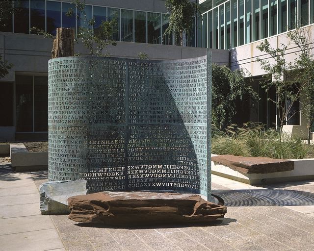 The full sculpture in the courtyard: the gently curving copper scroll, with petrified wood and granite slabs set at its foot.