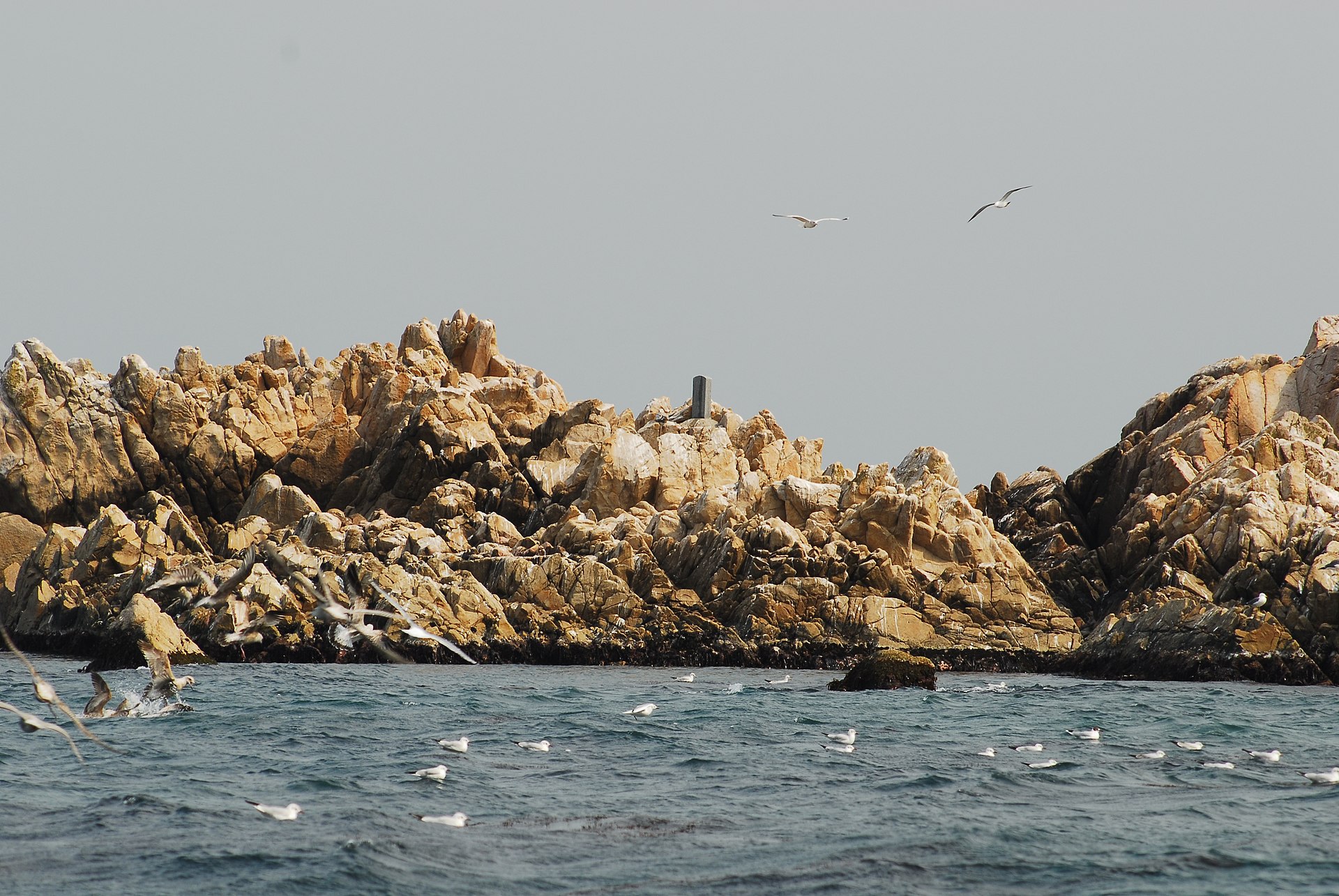 A distant view of Daewangam, waves surging into the channel between its rocks