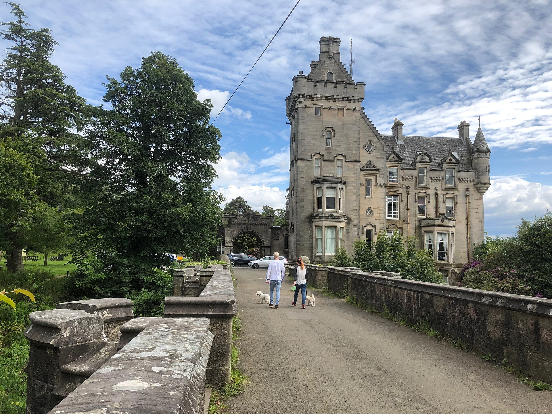 The low stone parapet of Overtoun Bridge, with a walker and their dog crossing it — a photograph of the actual bridge