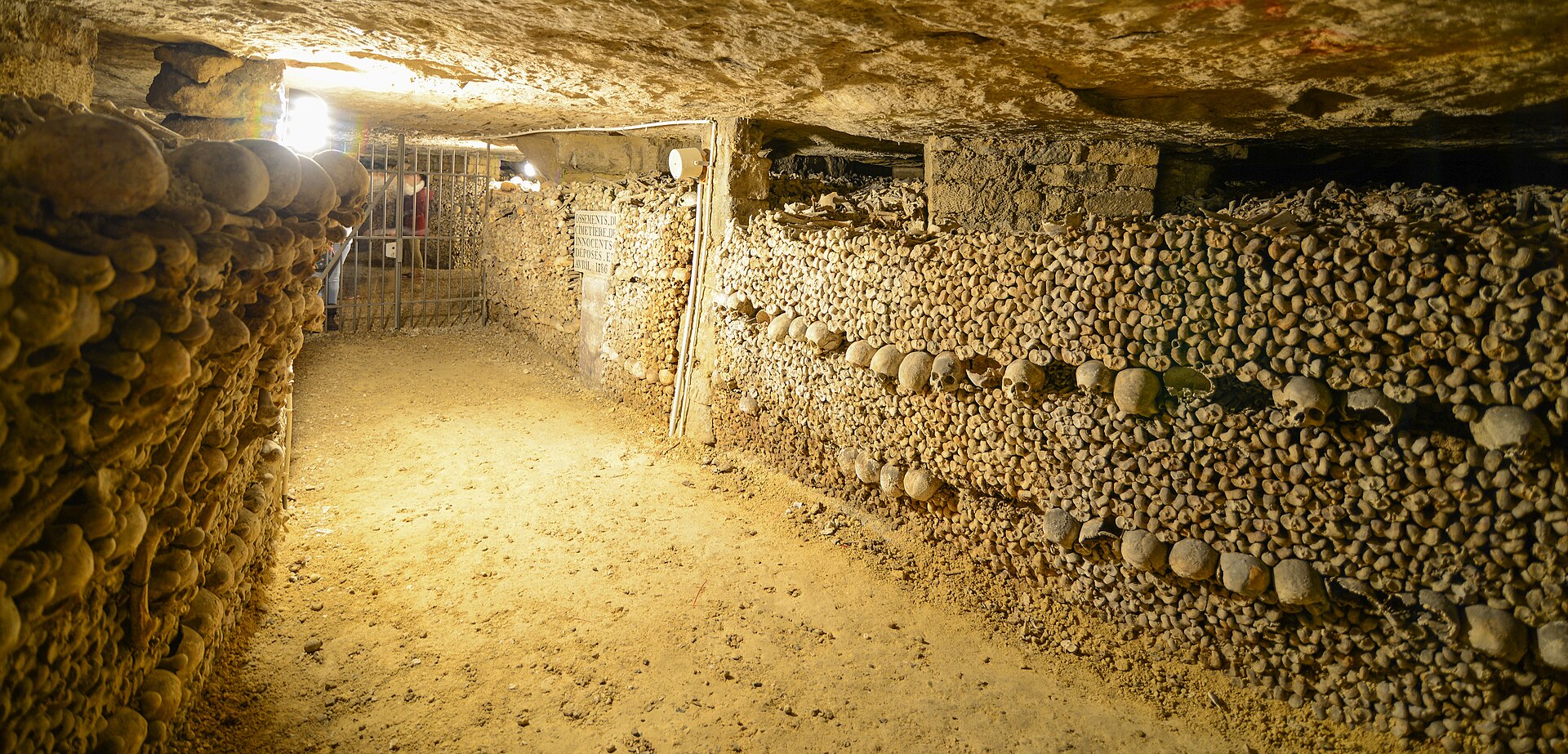A panoramic view of an ossuary gallery, skulls and femurs filling the walls on both sides