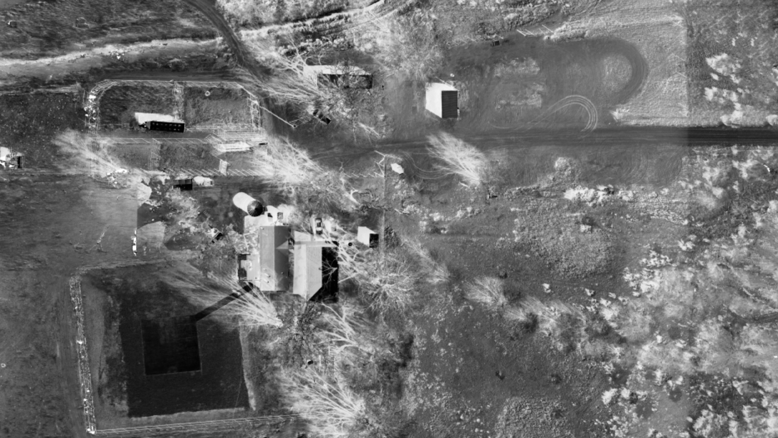 A black-and-white vertical aerial photograph of the Skinwalker Ranch headquarters area, showing the farmhouse, outbuildings and vehicle tracks