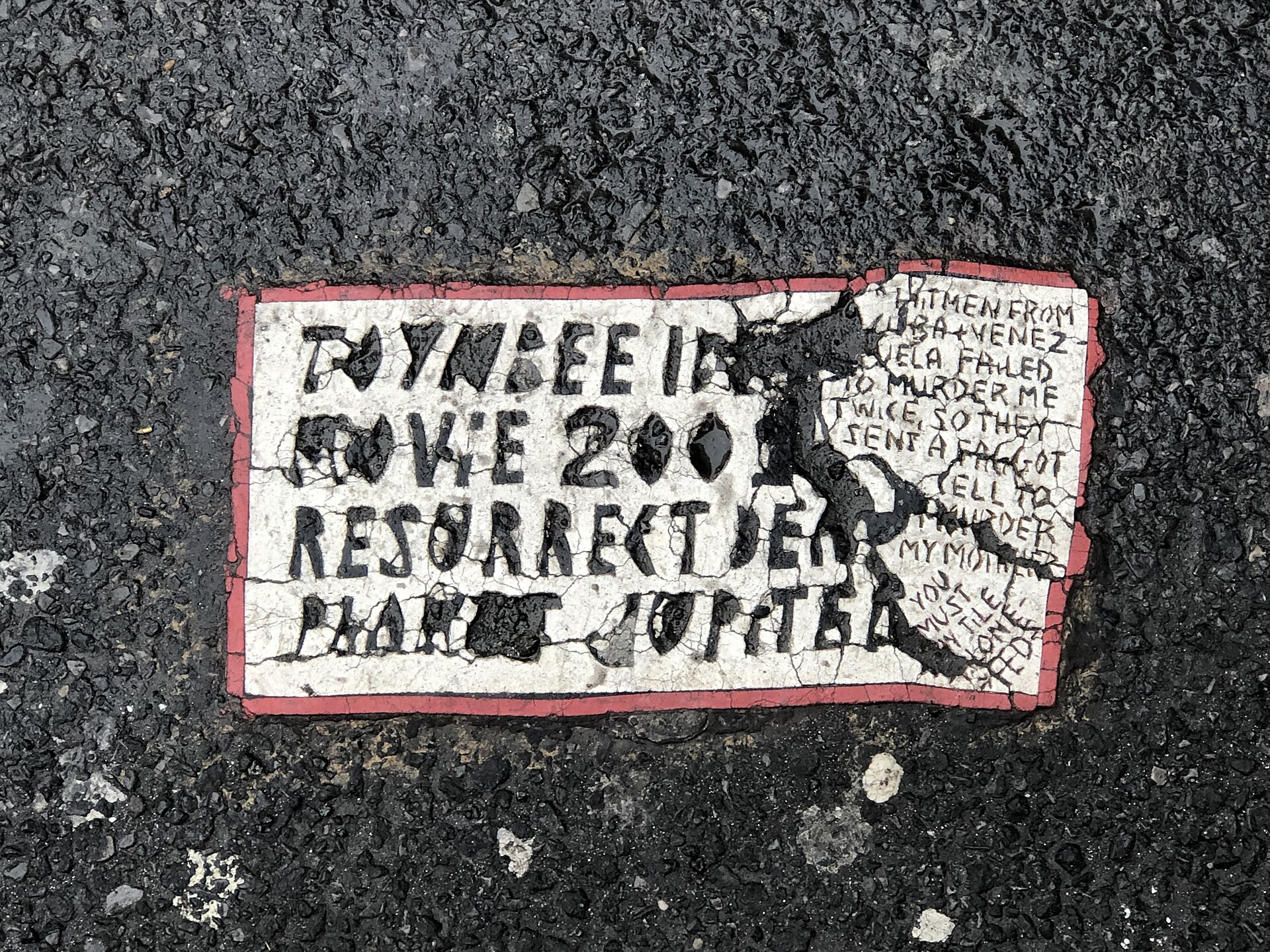 A Toynbee tile on W 43rd St, Manhattan — its right edge crowded with an agitated side text railing against the press and the government