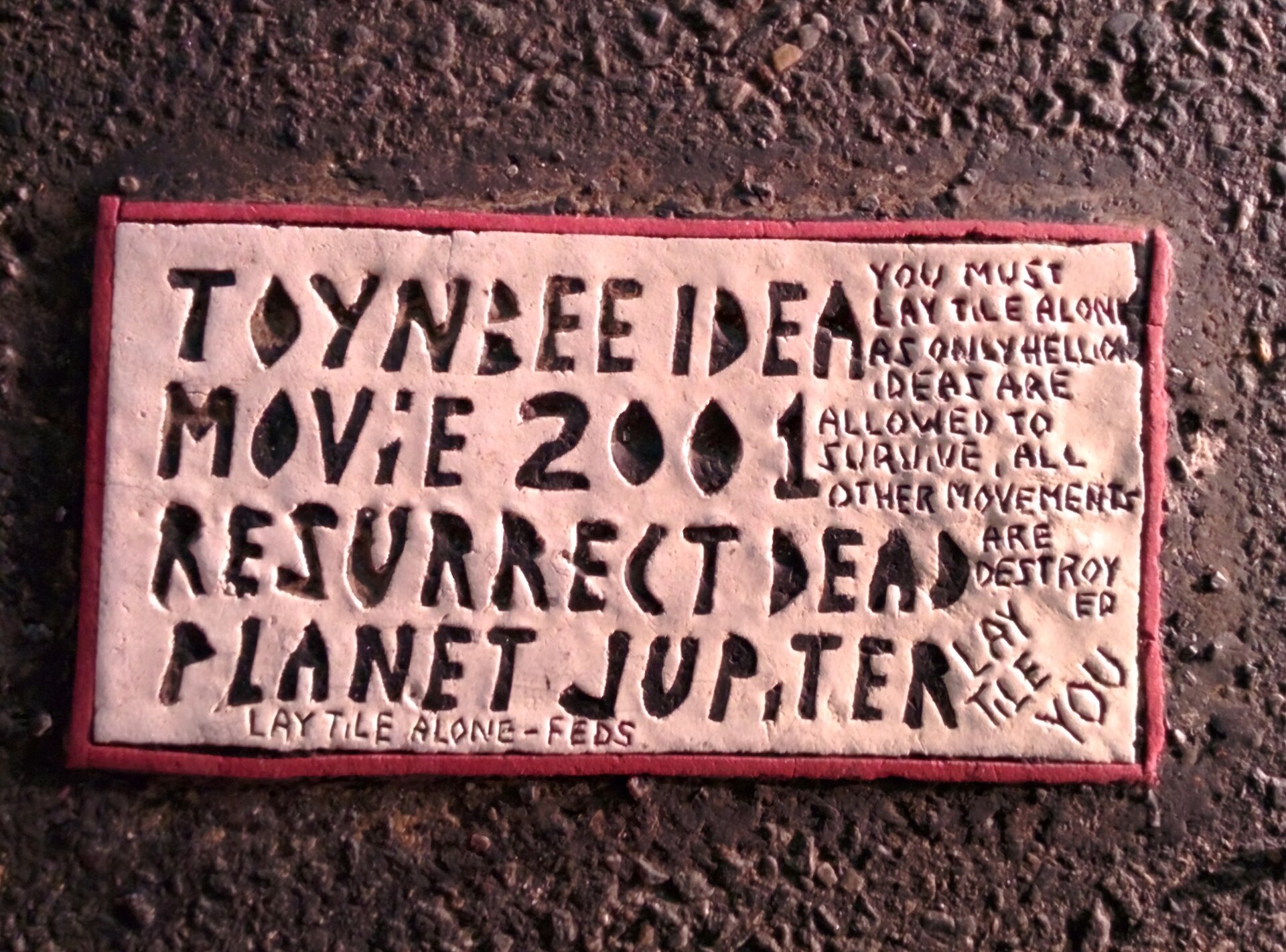 A close view of the tile at 38th and 5th Ave in New York — the standard text "Toynbee idea in movie 2001 resurrect dead on planet Jupiter" alongside the warning to lay tile alone