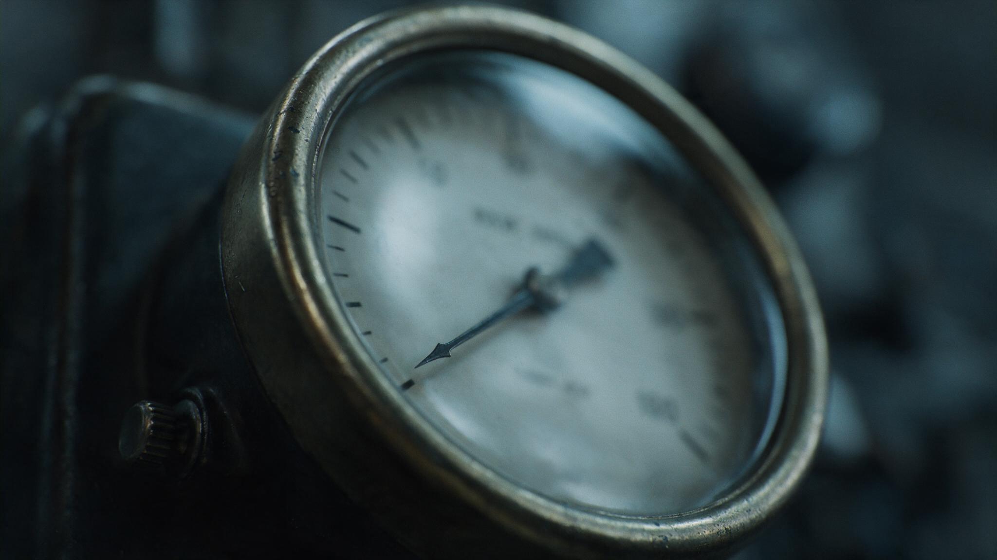 A close-up of an old analog dial and needle gauge in dim light, the needle resting near zero, cold and clinical, no legible text